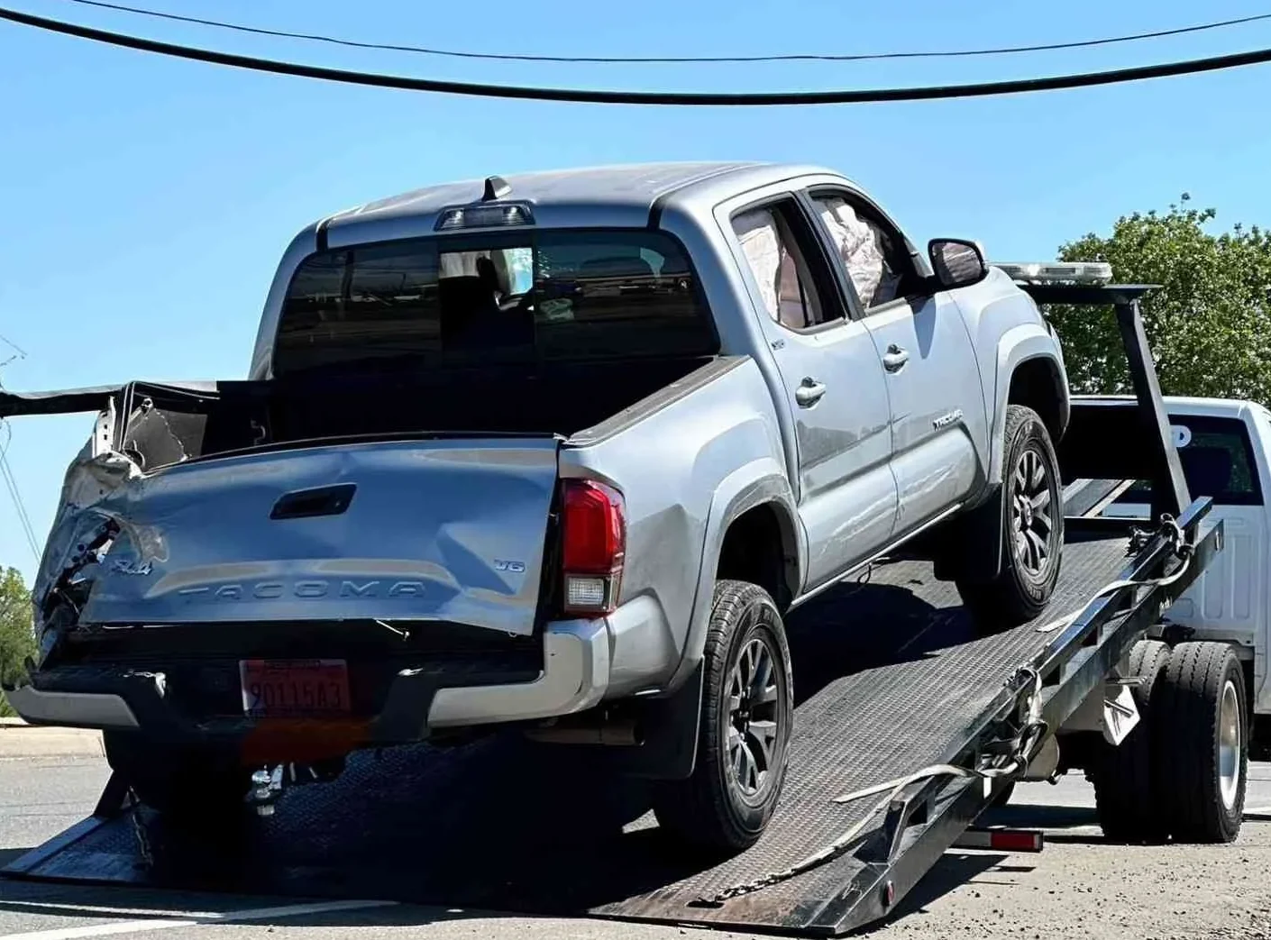 A silver pickup truck is being loaded onto a flatbed tow truck.