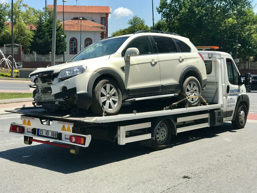 crashed white car being towed on a flatbed tow truck
